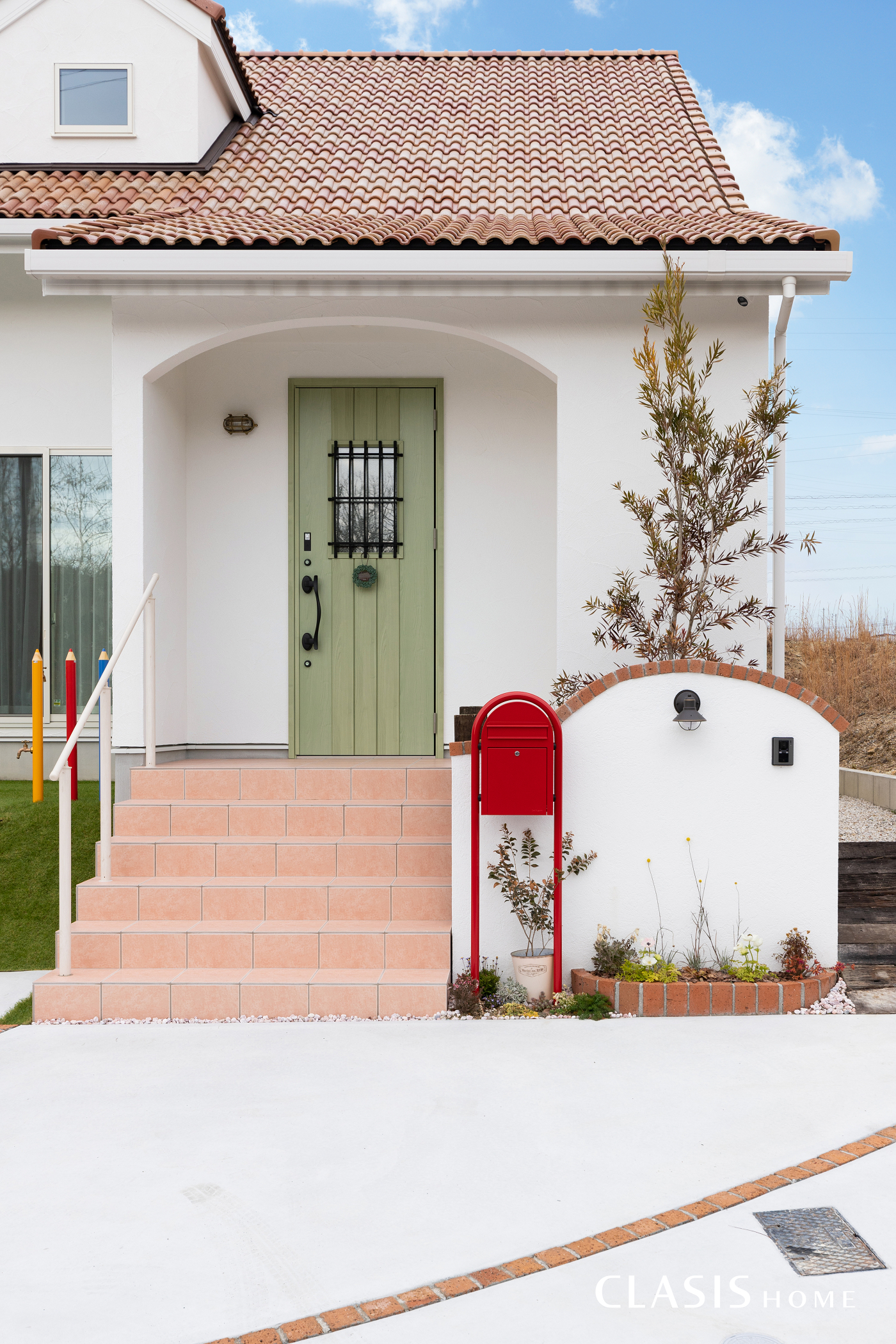 ドーマー屋根のお家の玄関周辺 白の塗り壁に、パステルグリーンの玄関扉や赤い郵便受けなど多彩な色遣い。