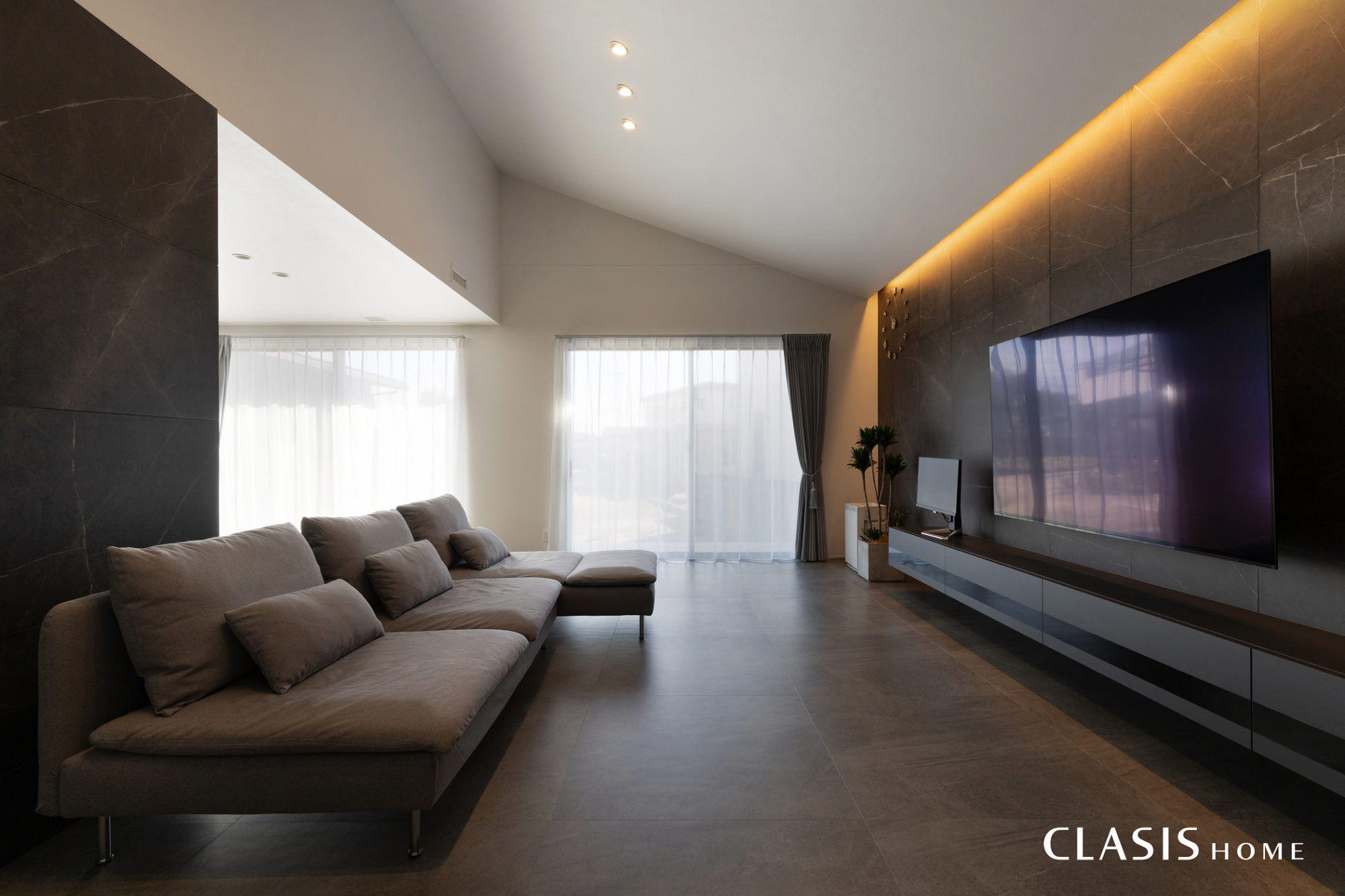 大判タイルのテレビ背面を、間接照明が柔らかく照らし、勾配天井が縦の伸びやかさを強調します。