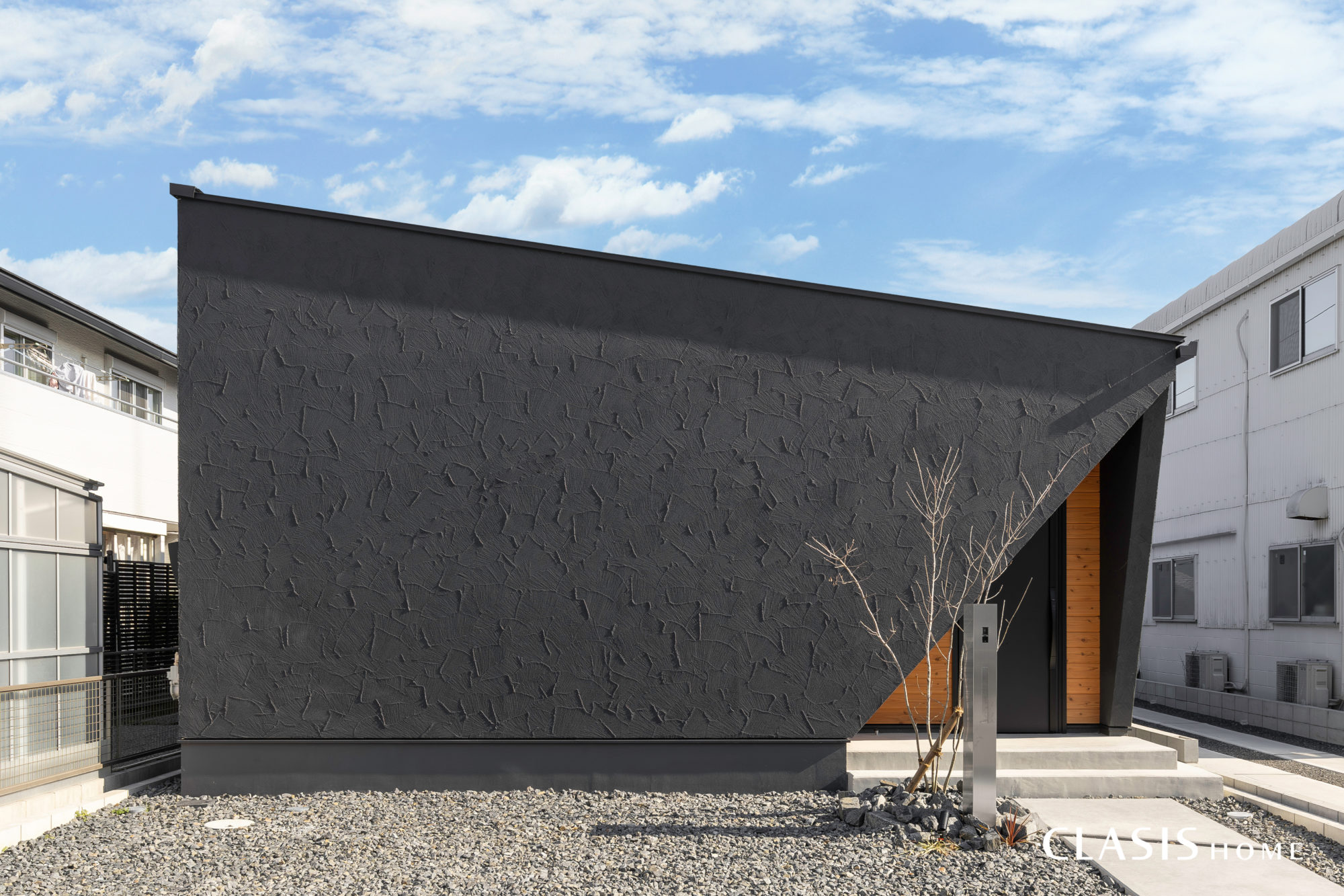 窓のないシンプルな箱型で黒の塗り壁と木目を組み合わせた平屋の外観。