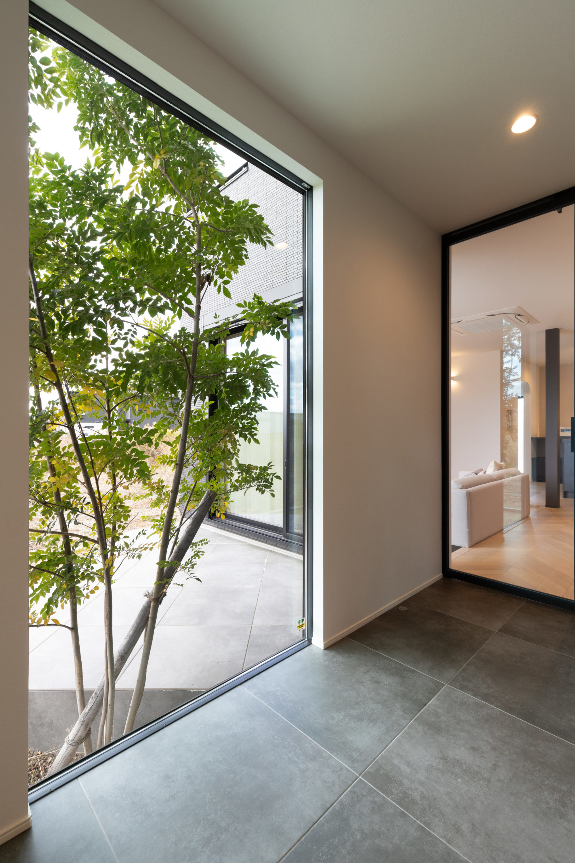 お庭と隣接する開放的な玄関ホール。ホールとリビングをガラス扉でつなげ、より広々とした空間を演出している。