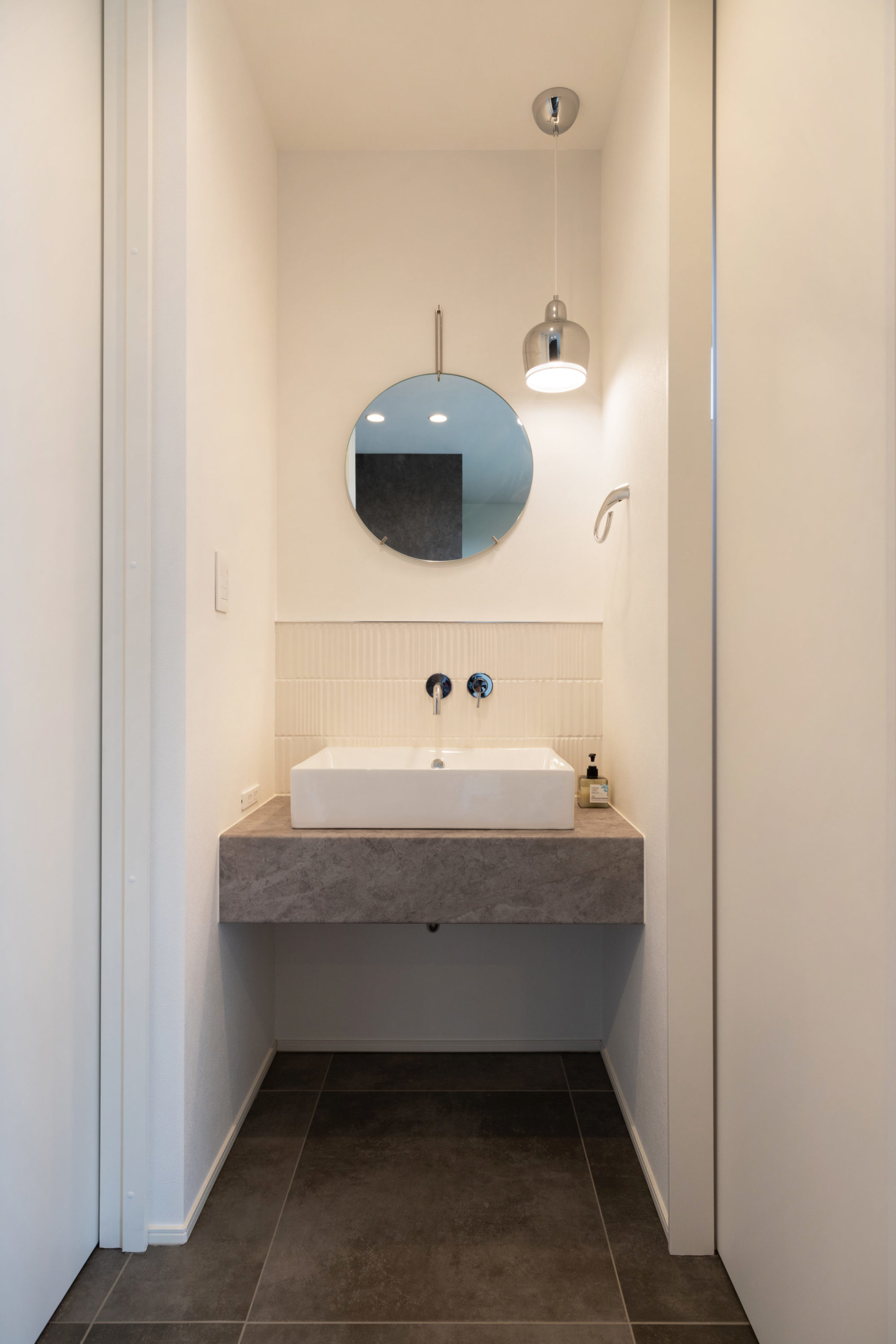 玄関ホールに設けた造作手洗い。モルタル調のカウンターとシルバーのアイテムが、スッキリとした印象。