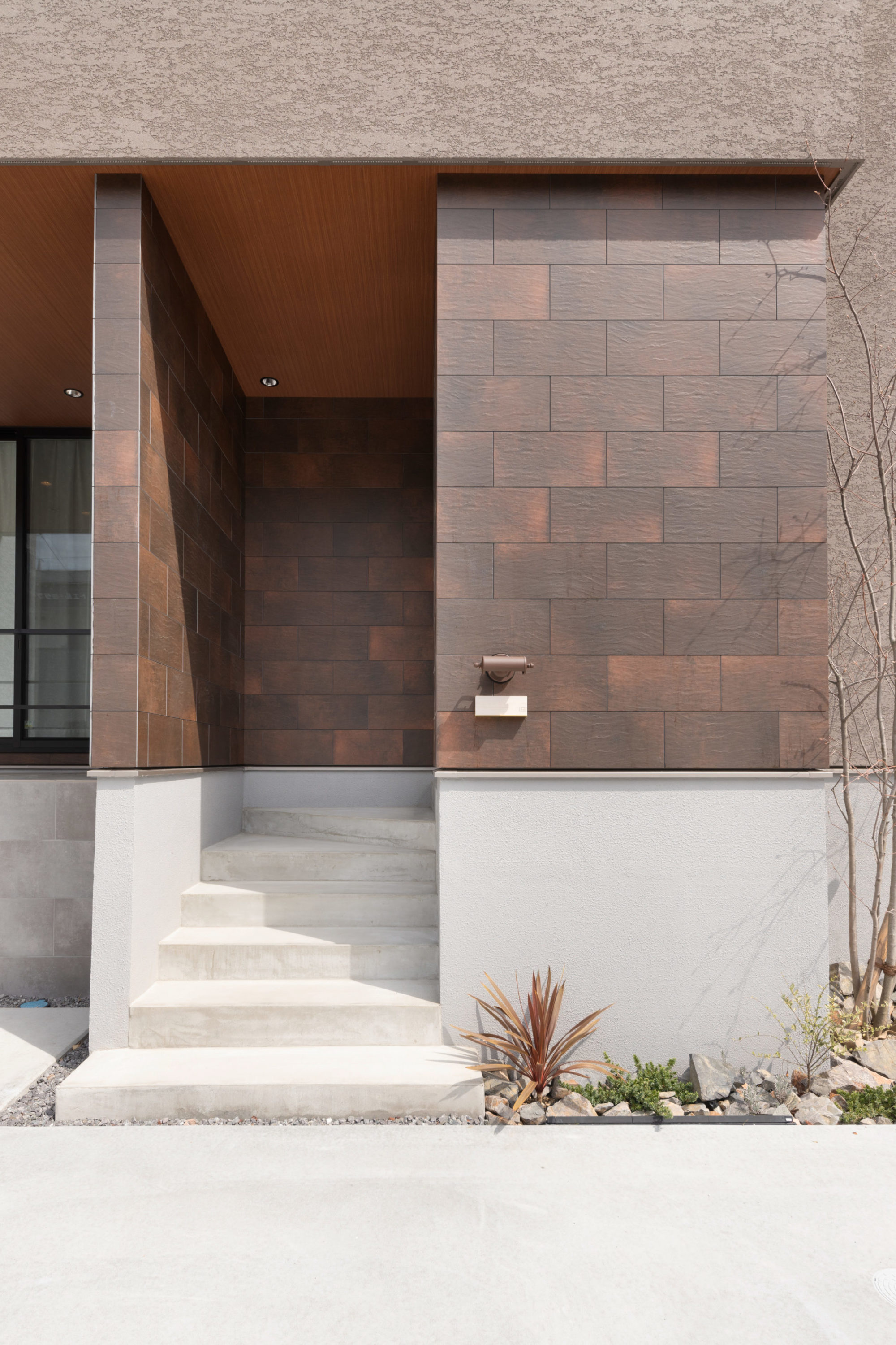 グラデーションのある質感が特徴の錆色のタイルを施した玄関ポーチ。