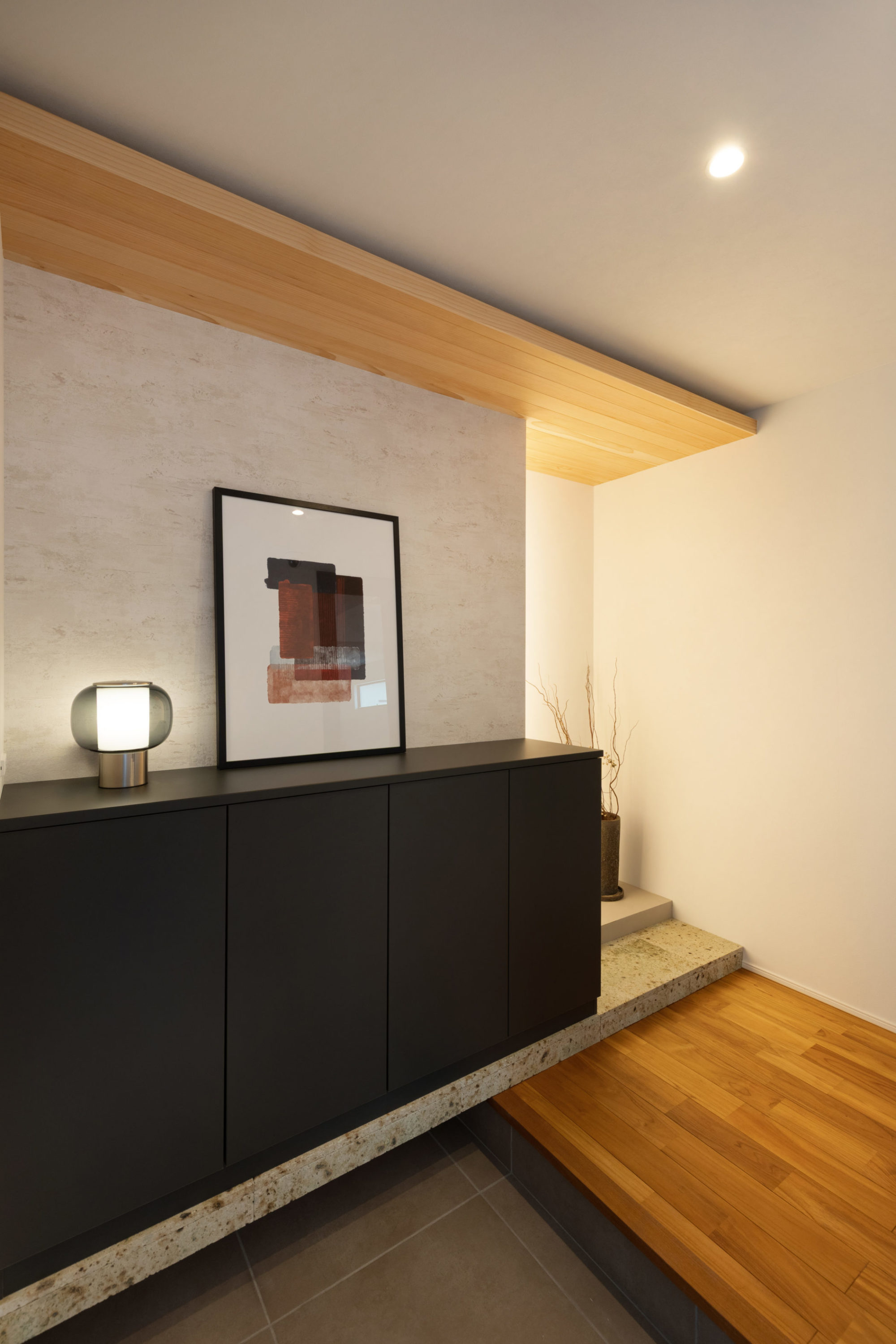 チークの無垢床と大谷石が調和する玄関ホール。床の間風ディスプレイスペースとヘムパネリング天井が和の趣を引き立てる空間。