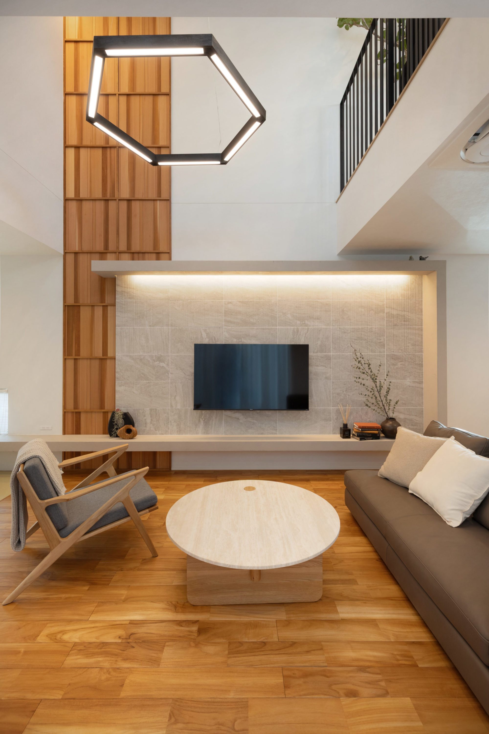 吹き抜けを彩るレッドシダーのパネリングと、間接照明がリブ形状のタイルを照らすテレビ壁面。壁面を囲うコの字型のフレームが飾り棚として機能する、意匠性の高いリビングデザイン。