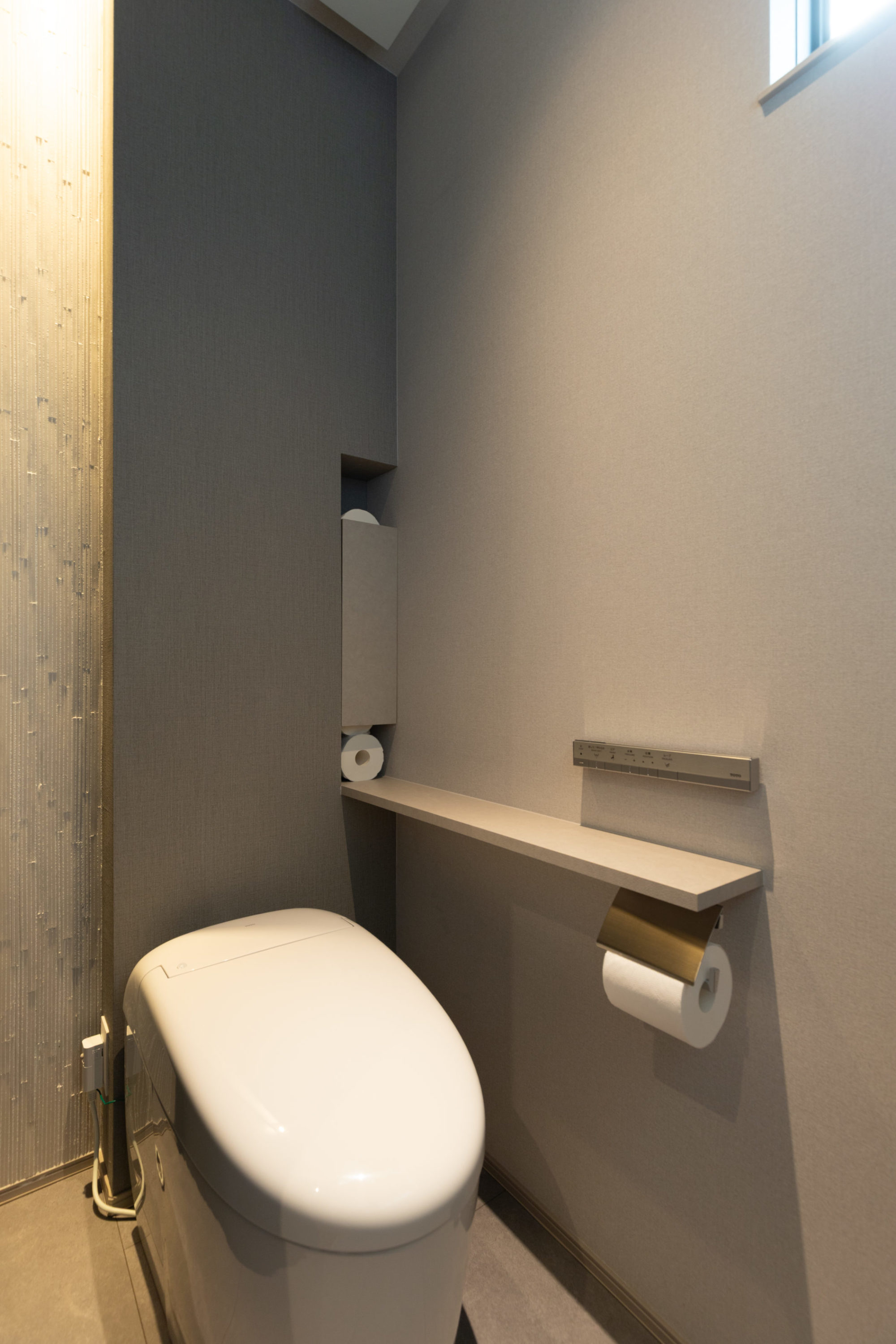 グレーを基調とした落ち着きのあるトイレ。奥の壁にあしらわれた縦ラインのタイルがアクセントとなり、コンパクトな空間にリズムと表情を与えるデザイン。