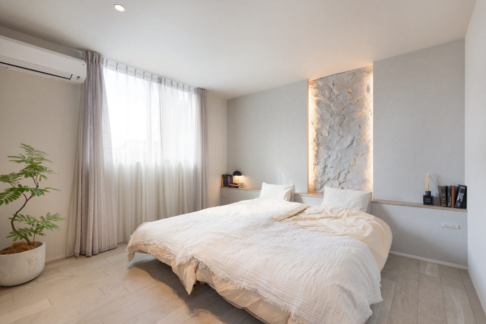 ベージュトーンでまとめた落ち着きのある主寝室。職人の手仕事による凹凸が美しいベッド背面のモルタル造形と、豊かな表情を持つ石目調のフロアタイルが調和するデザイン。